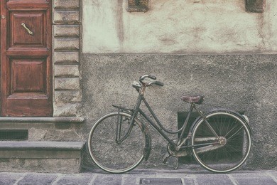 an old bicycle stands at the entrance stairway with a wooden door to the house in the little town of the italian region of tuscany