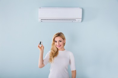 portrait of smiling young woman holding remote controller of air conditioner at home