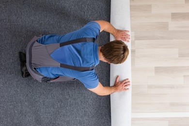 high angle view of male worker in overalls rolling carpet on floor at home