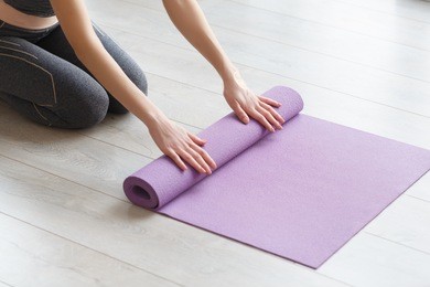 young yoga woman rolling her lilac mat after a yoga class on wooden floor near a window, close up