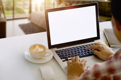man working with blank screen laptop on desk and workspace in living room.