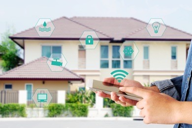 hand using smart phone as smart home control application over blurred house background, smart home concept
