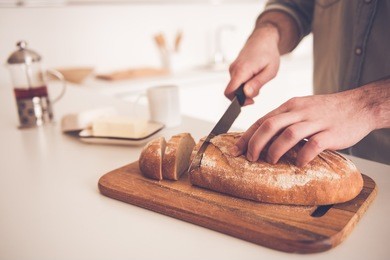 cropped image of handsome man cutting bread while doing sandwiches in kitchen at home