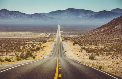 classic vertical panorama view of an endless straight road running through the barren scenery of the american southwest with extreme heat haze on a beautiful hot sunny day with blue sky in summer