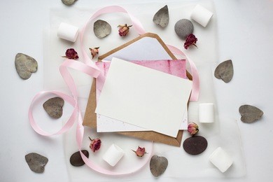 workspace. wedding invitation cards, craft envelopes, pink and red roses and green leaves on white background. overhead view. flat lay, top view wedding invitation card templates. 