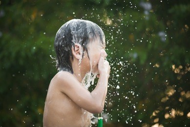 cute asian boy has fun playing in water from a hose outdoors