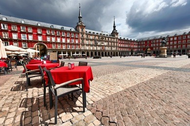 cafe tables with red tablecloths in plaza mayor against dramatic clouds. madrid. spain.