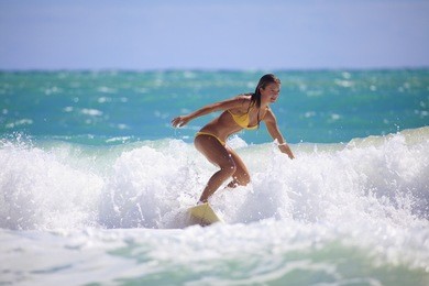 teenage girl in a yellow bikini surfing in hawaii