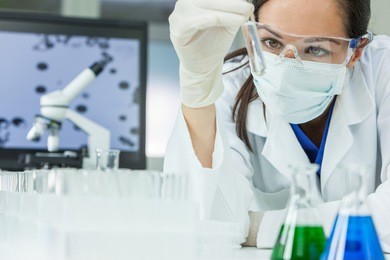 female medical or research scientist or doctor using looking at a test tube of clear solution in a lab or laboratory 