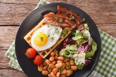 breakfast with fried egg, waffles, bacon, mix lettuce and beans close-up on the table. horizontal view from above