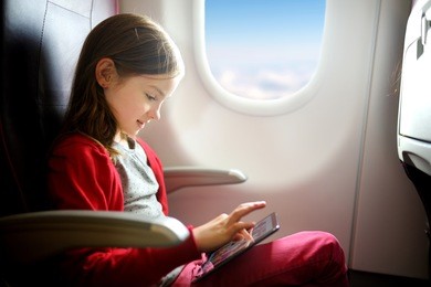 adorable little girl traveling by an airplane. child sitting by aircraft window and using a digital tablet during the flight. 