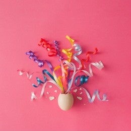 egg with party streamers on pink background. easter concept. flat lay.