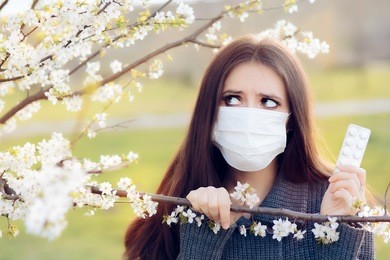 woman with respirator mask fighting spring allergies outdoor - portrait of an allergic woman surrounded by seasonal flowers wearing a protective mask

