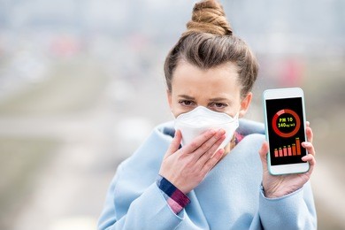 woman in protective mask holding smart phone with air polution measurement of pm10 outdoors