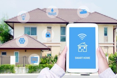 hand using tablet as smart home control application over blurred house background, smart home concept