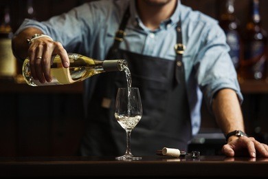 male sommelier pouring white wine into long-stemmed wineglasses.