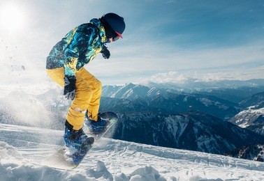 snowboarder is jumping with snowboard from snow hill in the sun beam