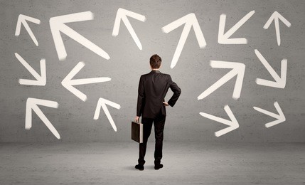 an elegant businessman standing with his back in front of urban wall full of arrows pointing in different directions concept