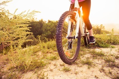 girl on mountain bike rides on the trail on a beautiful sunrise. bicycle wheel closeup