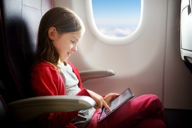 adorable little girl traveling by an airplane. child sitting by aircraft window and using a digital tablet during the flight.