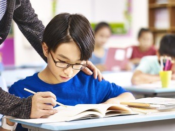 asian elementary school boy getting help from teacher in class.