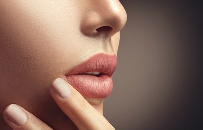 beauty fashion woman lips with natural makeup and beige nail polish. matte lipstick and nails. beauty girl face close up. nude colors. sexy lips, manicure, make up. over brown background.