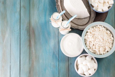 tasty healthy dairy products on a table on a blue background: sour cream, cottage cheese, mozzarella cheese, butter,ricotta and milk in a bottle