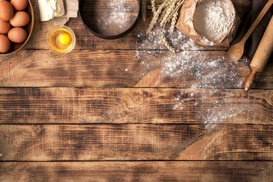 flour with wheat, eggs, rolling pin, spoon and butter on wooden background, top view with copy space. ingredients for bakery products