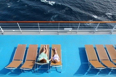 mother and daughter lying on beach armchairs on cruise liner deck, view from above