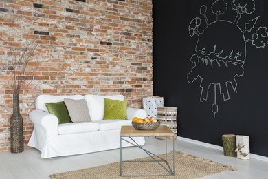 living room with white couch, pillows, chalkboard and brick wall