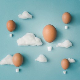 hot air balloons made of easter eggs with cotton clouds on bright blue background. flat lay. creative concept.