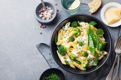 pasta with green vegetables and creamy sauce in black bowl on grey stone background. top view. copy space.