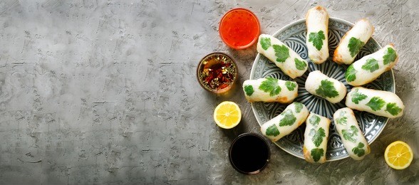 fresh vietnamese, asian, chinese food frame on grey concrete background. spring rolls rice paper, lettuce, salad, vermicelli, noodles, shrimps, fish sauce, sweet chili, soy, lemon. top view