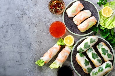 fresh vietnamese, asian, chinese food frame on grey concrete background. spring rolls rice paper, lettuce, salad, vermicelli, noodles, shrimps, fish sauce, sweet chili, soy, lemon. top view
