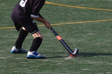 child field hockey player hits the ball hard while playing on sandy turf field