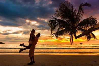romantic couple on the tropical beach at background colorful sunset
