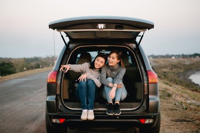 two happy asia woman friends enjoying road trip in hatchback car,flare light
