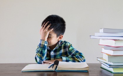 tired asian kid when doing homework and stack of book on the wooden table