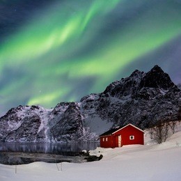 lofoten, svoelver, aurora borealis over a frozen lake and red rorbu, norway.