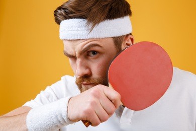 image of handsome young sportsman dressed in white t-shirt standing isolated over yellow background holding racket for table tennis. looking at camera.
