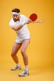 image of concentrated emotional young sportsman dressed in white t-shirt standing isolated over yellow background holding racket for table tennis. looking at camera.