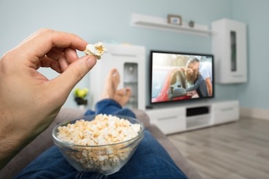 close-up of a person enjoy watching movie on television while eating popcorn
