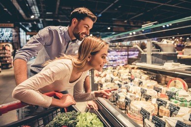 beautiful young couple is choosing cheese and smiling while doing shopping at the supermarket