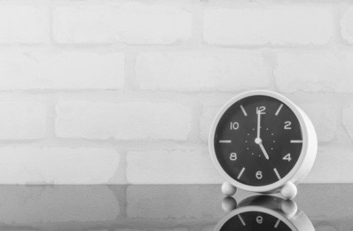 closeup black and white alarm clock for decorate in 5 o'clock on black glass table and white brick wall textured background in black and white tone with copy space