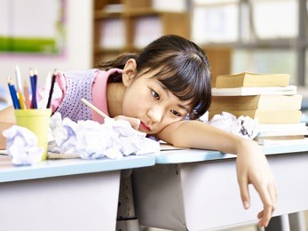 asian elementary school girl frustrated after several failed attempts while writing an essay.