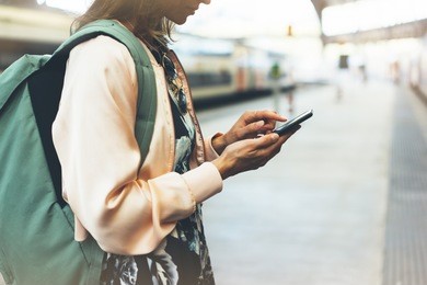 enjoy travel. young pretty woman waiting on the station platform with backpack on background electric train using smart phone. tourist text message plan route of railway, railroad transport concept