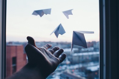 a man's hand lets go little paper planes out of window to nowhere