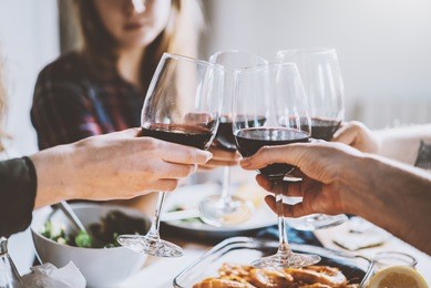 happy friends making cheers with glasses of red wine, group of people celebrating anniversary at home, cozy atmosphere, family dinning at restaurant, togetherness and traditional concept