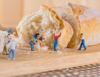 concept idea image of mini figure dolls  making french baguette bread on slice board.