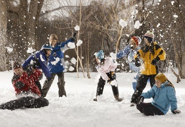four people outdors in hats, coats and scarves, having an energetic snowball fight,